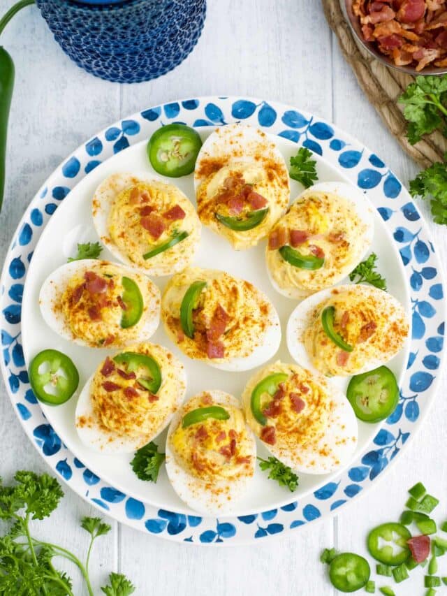 Spicy deviled eggs on a plate sprinkled with red pepper and jalapenos.