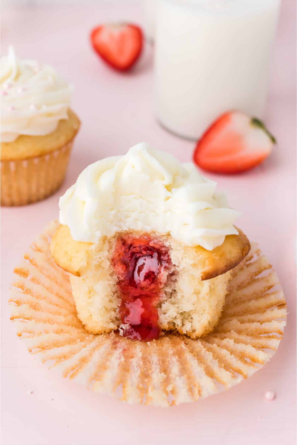 Strawberry cupcake on a paper liner with a bite missing.