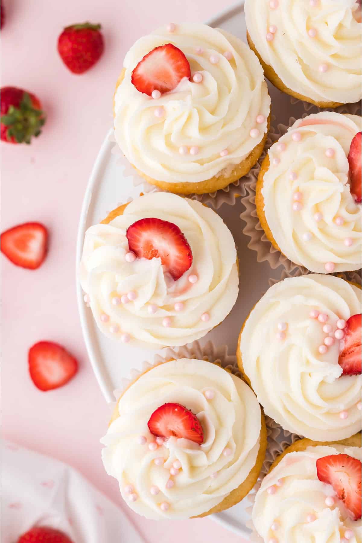 A plate of strawberry filled cupcakes with icing and strawberries for garnish.