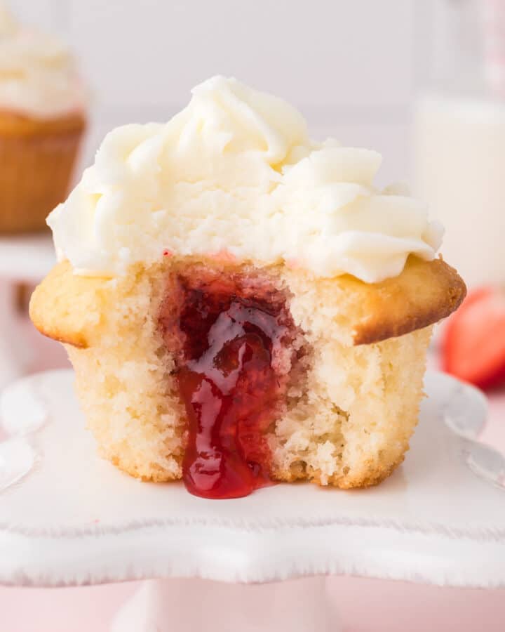 A strawberry filled cupcake with bite missing and the filing spilling out.