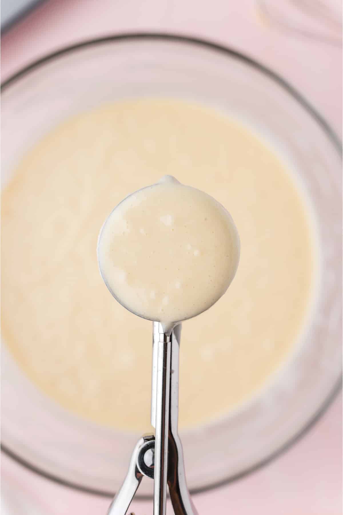 A scoop filled with batter over the bowl of cupcake batter.