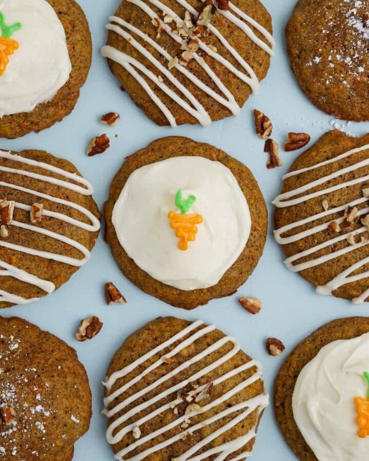 Carrot cake cookies directly on a blue background with little cookie bits and cream cheese frosting on top of the cookies.