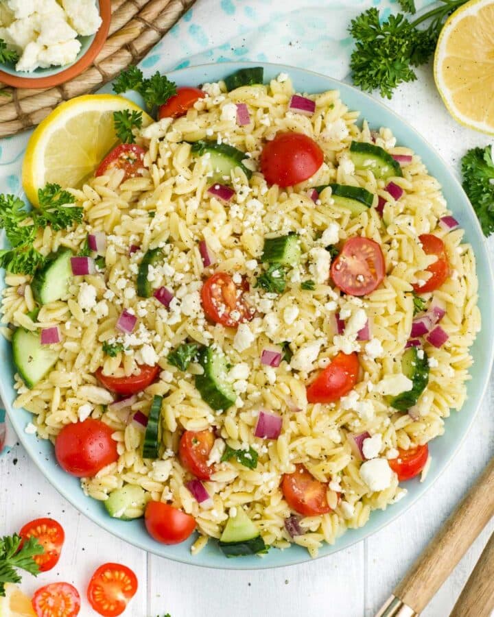 Lemon orzo salad in a blue bowl with spoons on the table to the side.
