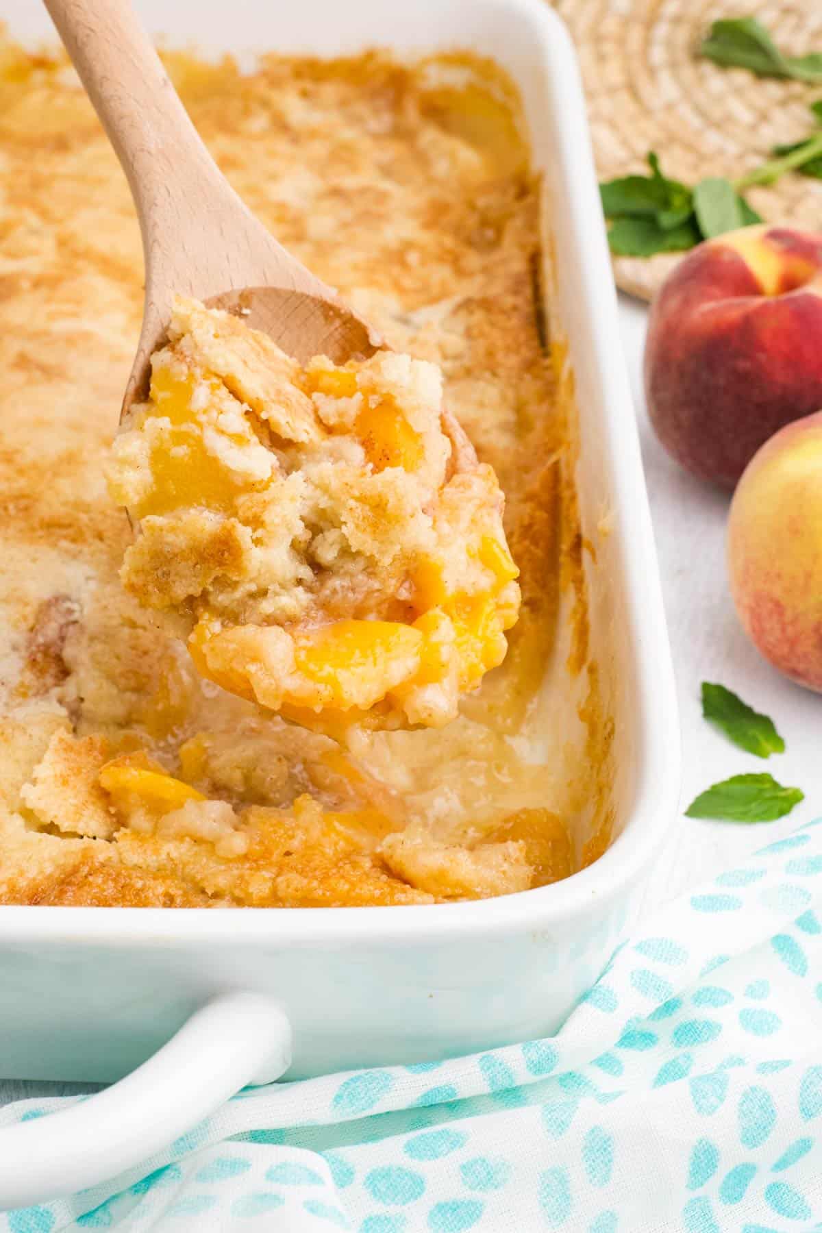 Peach dump cake with a wooden spoon scooping up a portion.