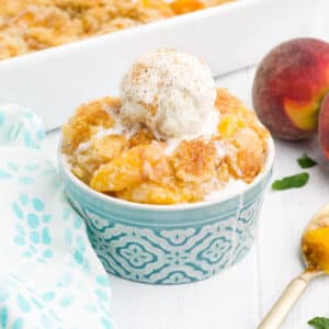 Bowl of peach cobbler with cake mix topped with a scoop of ice cream.