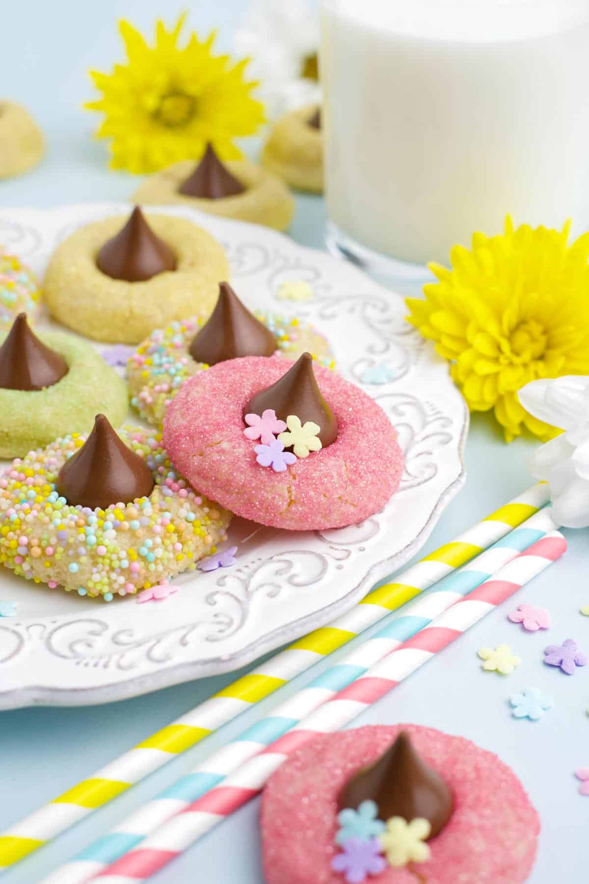 Spring blossom cookies on a white plate with a yellow straw and pastel colored straws beside the plate.