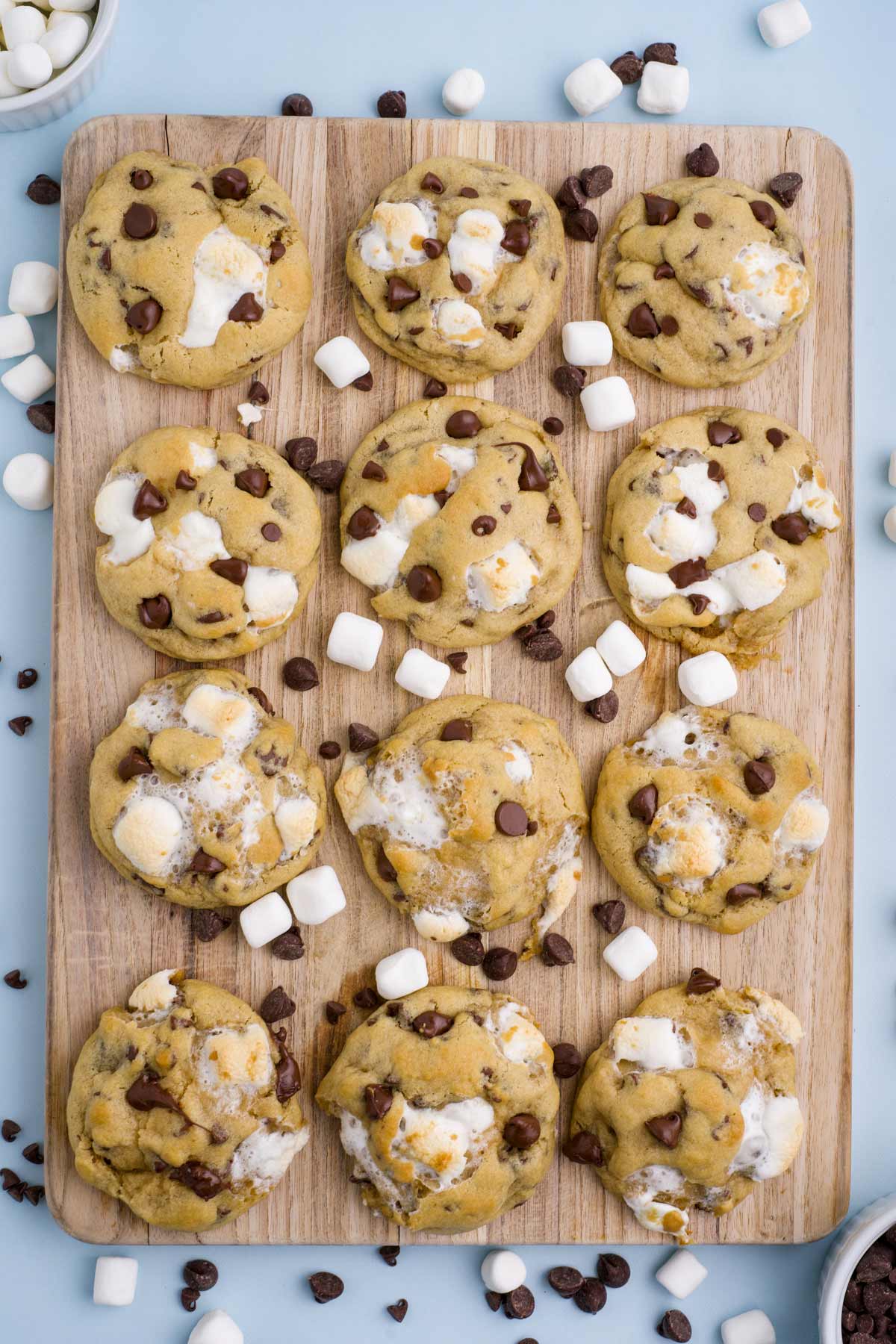 Cookies laid out flat on a cutting board with marshmallows and chocolate chips sprinkled around.