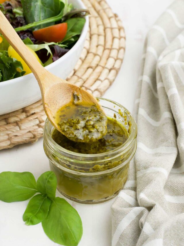 Pesto dressing in a small glass jar with a spoon in it.
