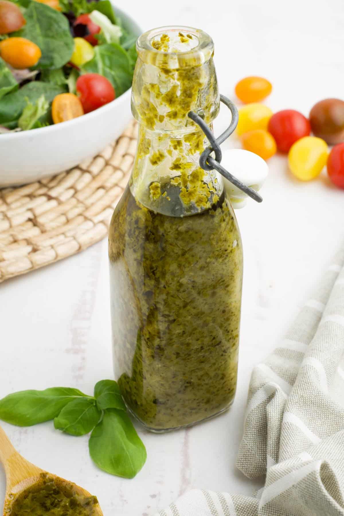 A bottle of pesto salad dressing on the table in front of a bowl of salad.
