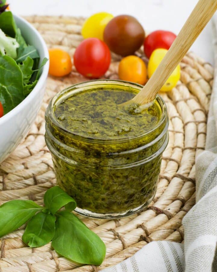A small jar of pesto salad dresinng on the table with a spoon in it.