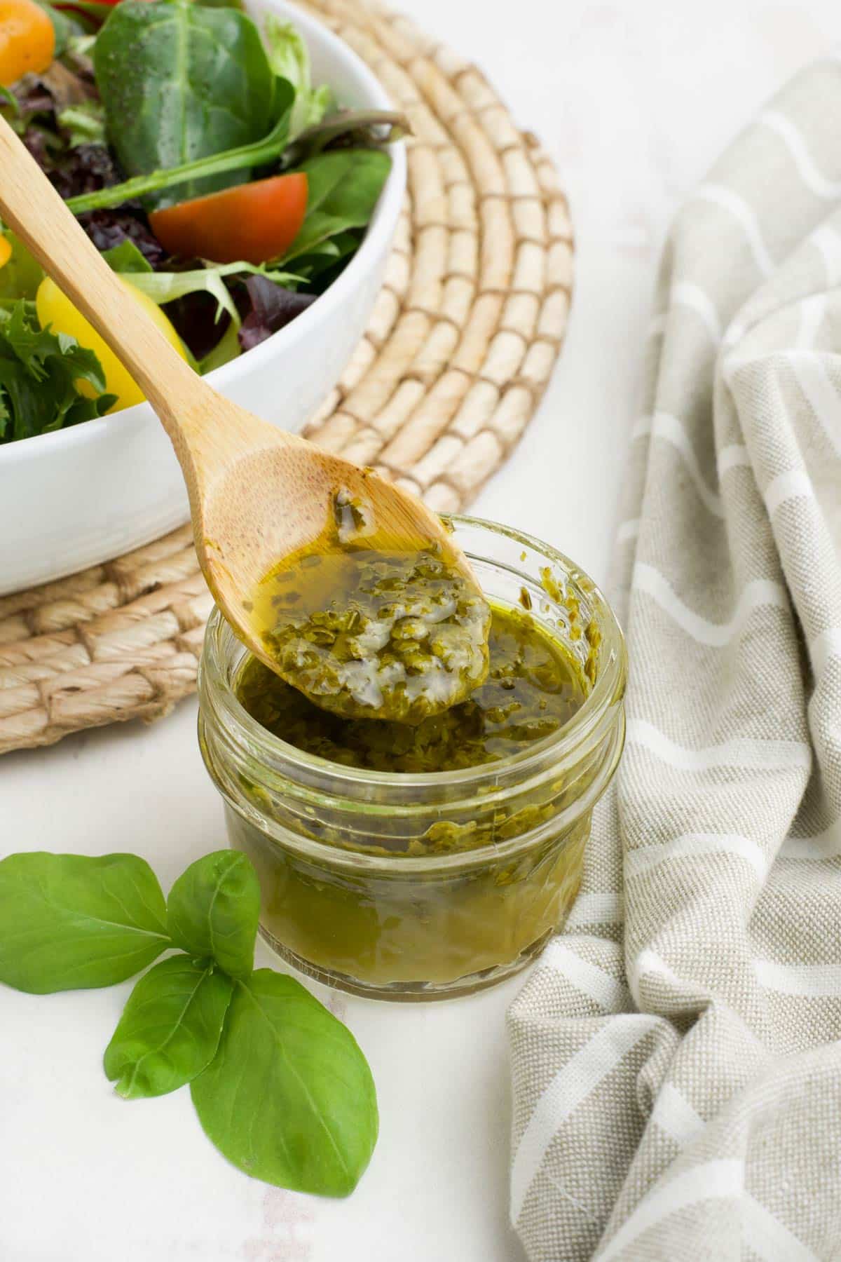 Pesto dressing in a small glass jar with a spoon in it.