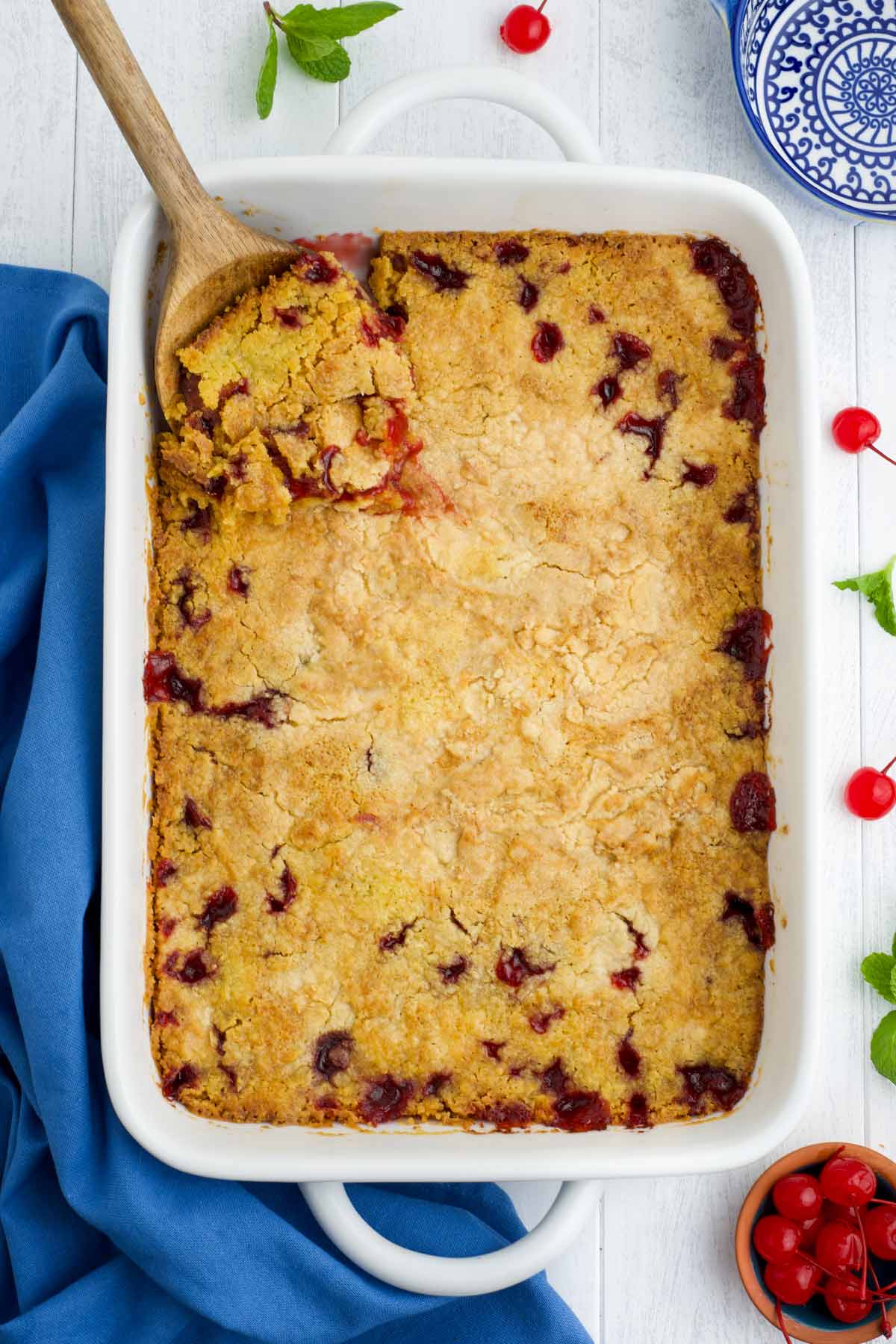 A freshly baked cherry dump cake with a wooden spoon dipping into a corner.
