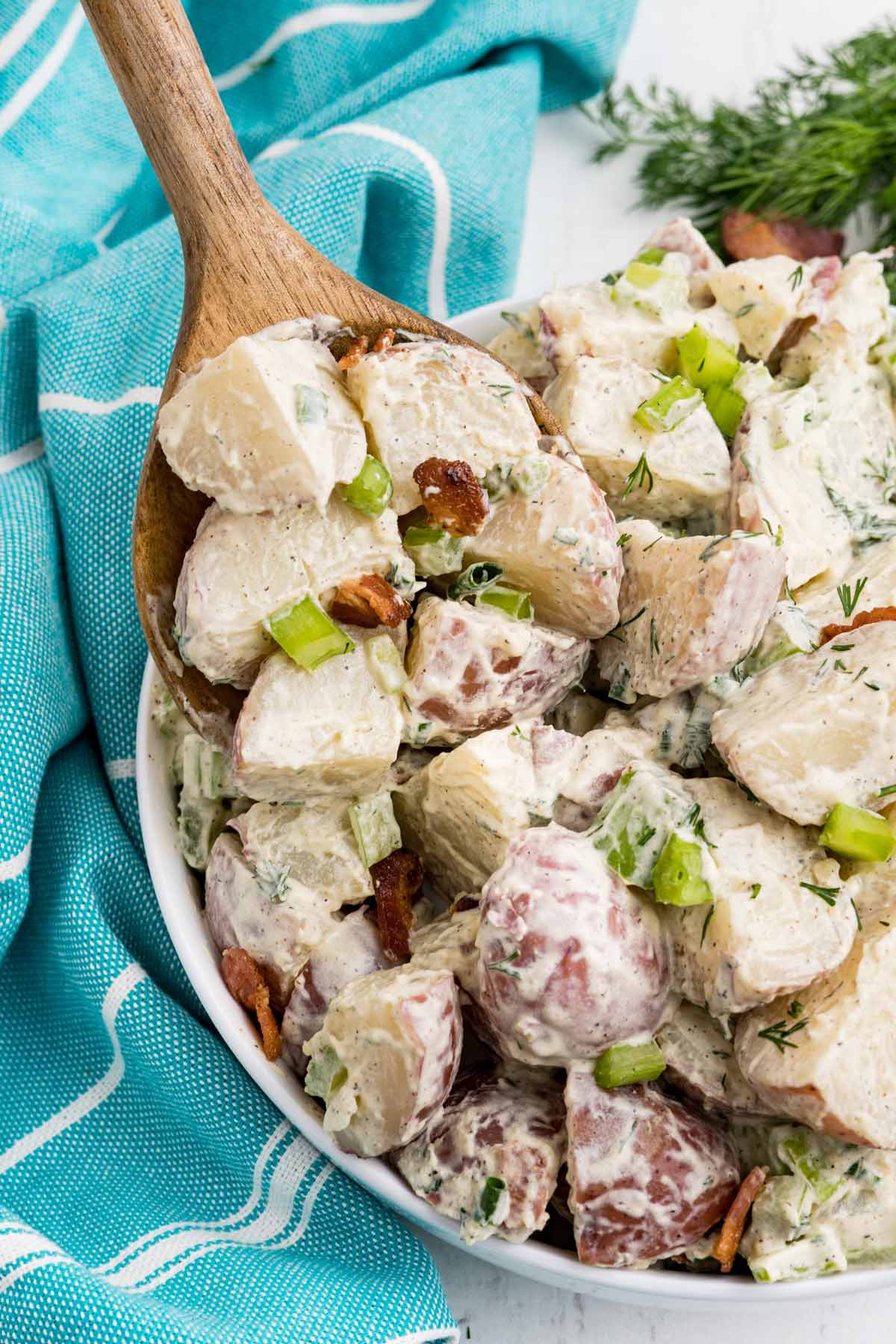 A wooden spoon scooping out a serving of bacon potato salad.