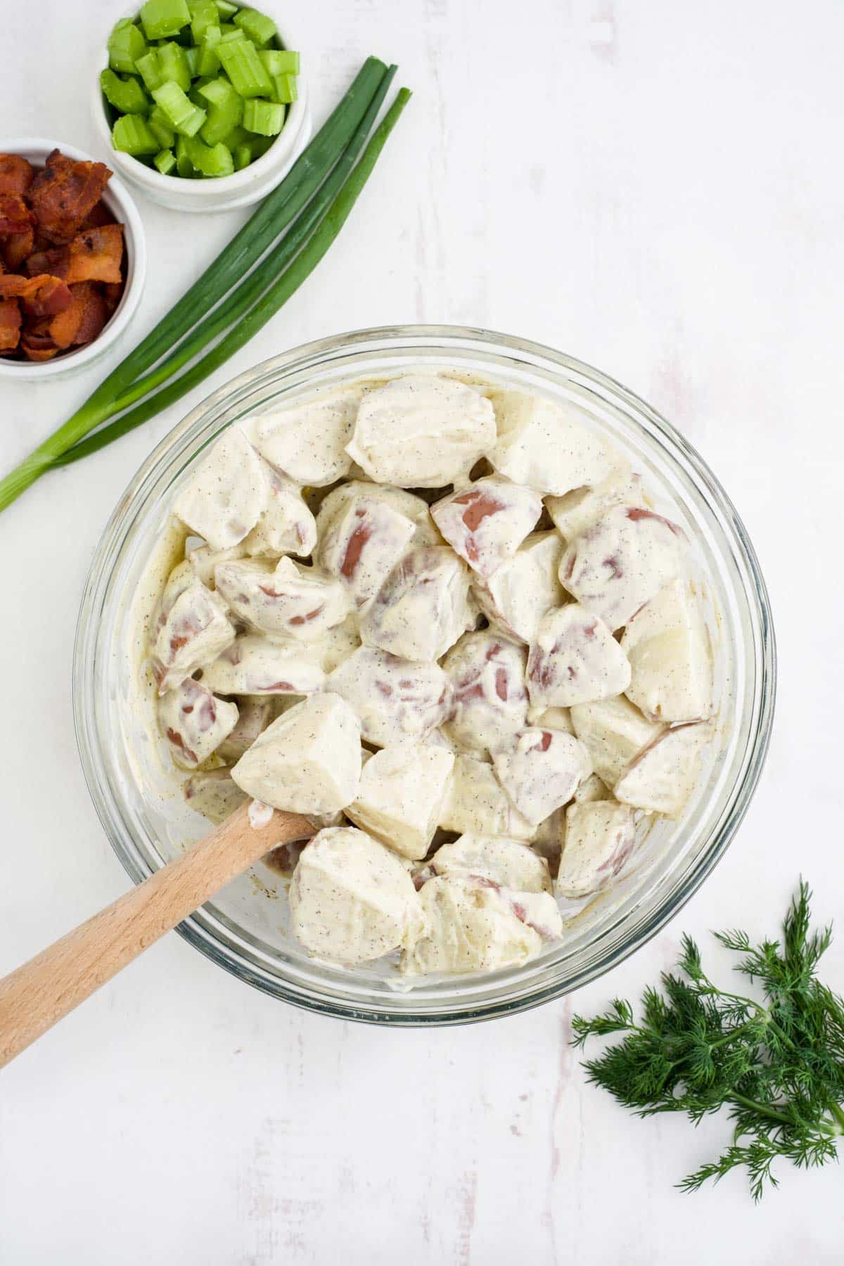 Dressing added to the cooked potatoes in a bowl.