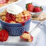 A small dish of strawberry dump cake served up on the table with fresh berries and whipped cream.