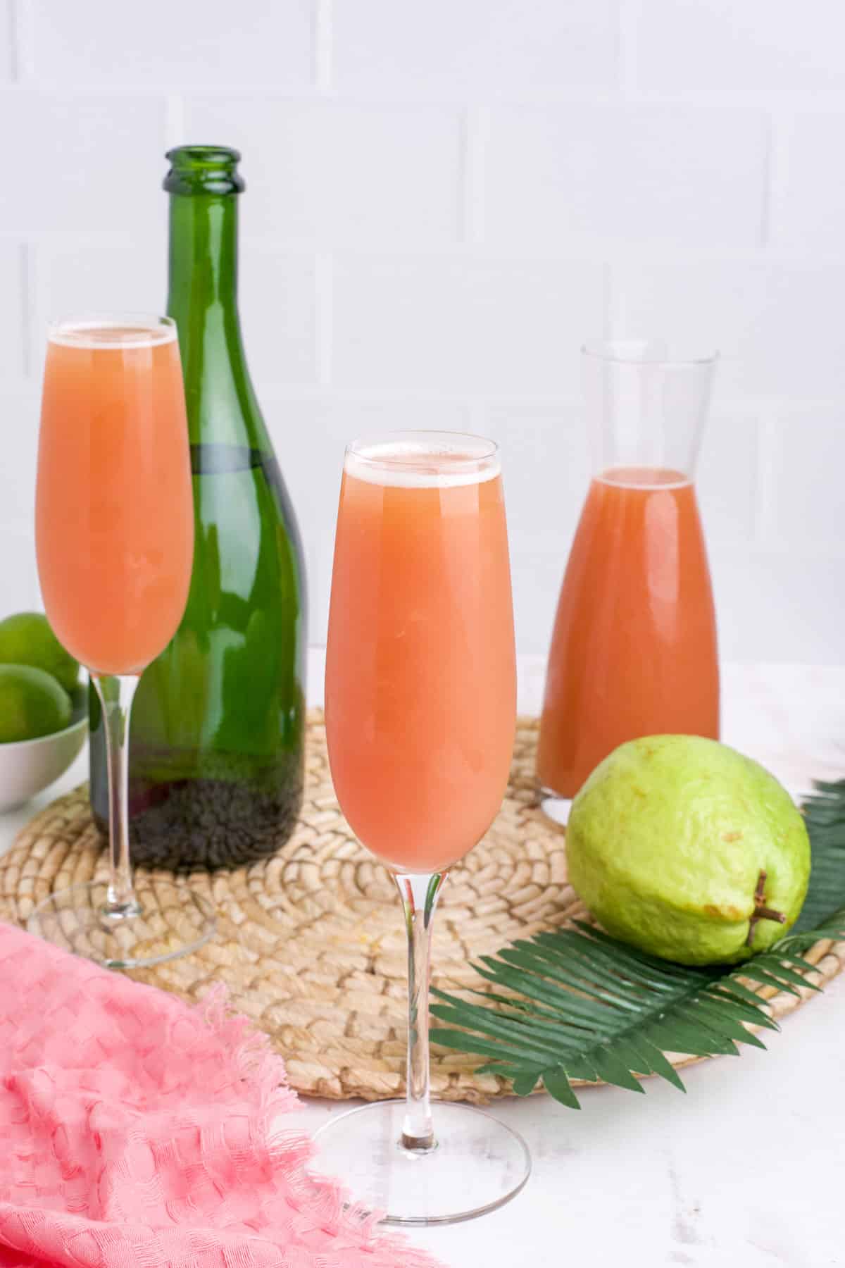 Guava mimosas on the table with a carafe of guava juice and bottle of champagne in the background.