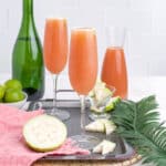 Glasses of guava mimosas on a serving tray with fresh guava.