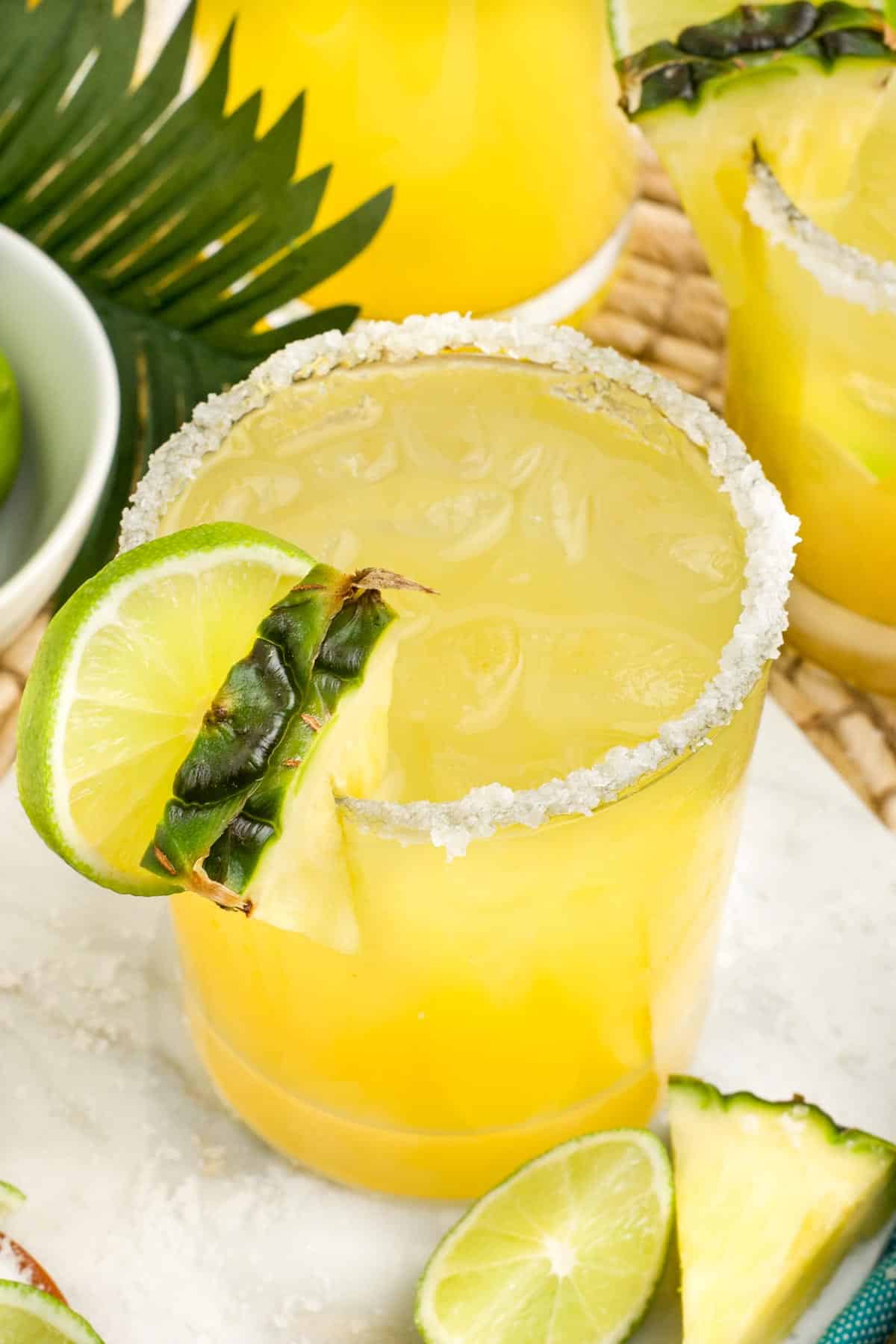 A pineapple margarita in a salted glass with a lime and pineapple on the glass edge.