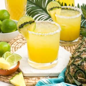 A glass of pineapple margarita on the table with fresh limes and pineapple.