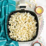 Air fryer basket on the table with freshly popped popcorn.