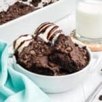 A bowl of chocolate dump cake topped with ice cream and chocolate sauce on the table.
