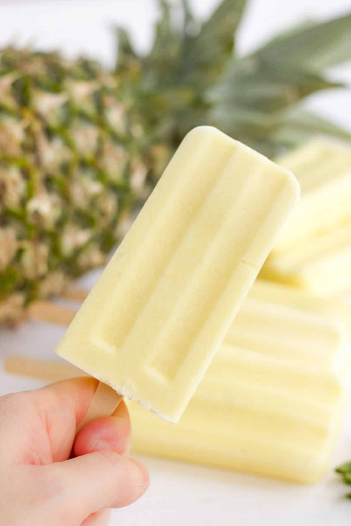 A hand holding a dole whip popsicle over the table.