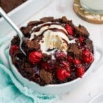 Chocolate cherry dump cake in a bowl with a blue napkin on the side and ice cream on top with a spoon.