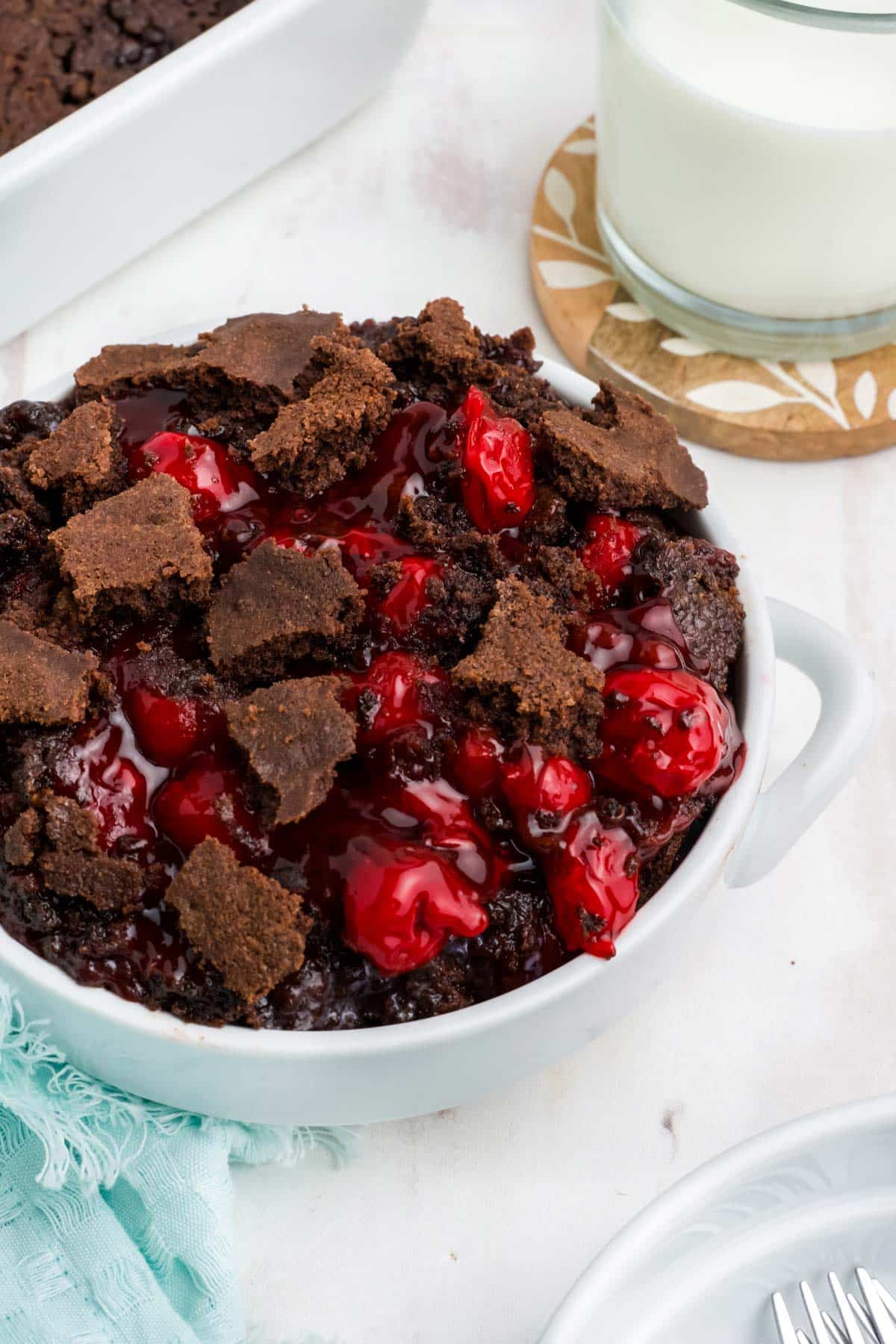 Chocolate cherry dump cake served up in a white bowl on the table.