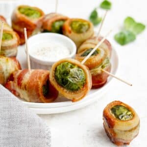 Bacon wrapped brussels sprouts on the table on a plate with a sauce in the middle.