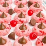 Cherry blossom cookies lined up on a tray with cherries and chocolate kisses around them.