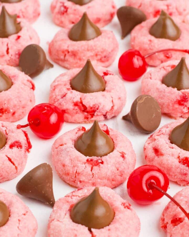 Cherry blossom cookies lined up on a tray with cherries and chocolate kisses around them.