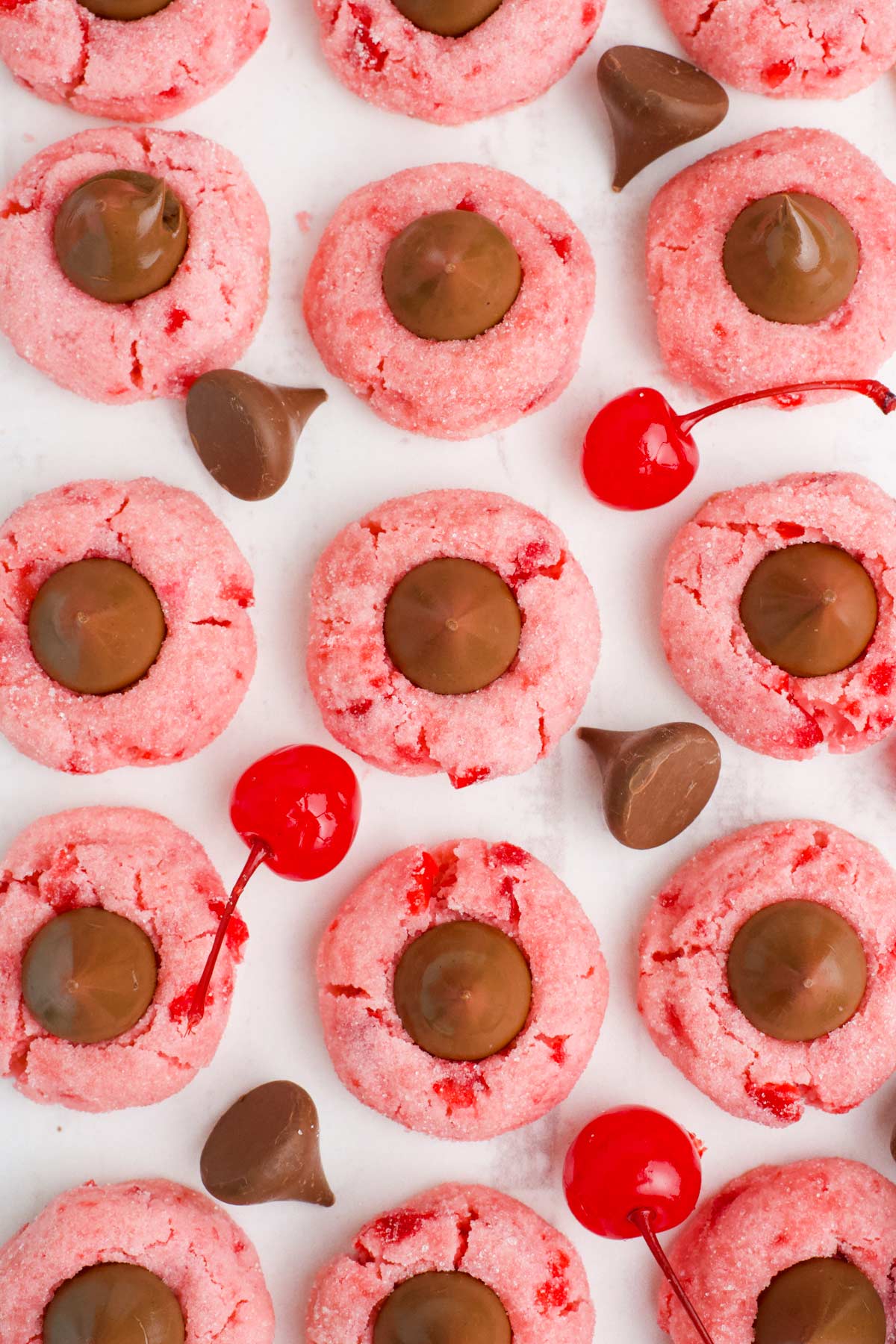 Overhead image of cherry blossom cookies on a white surface with cherries and kisses around them.