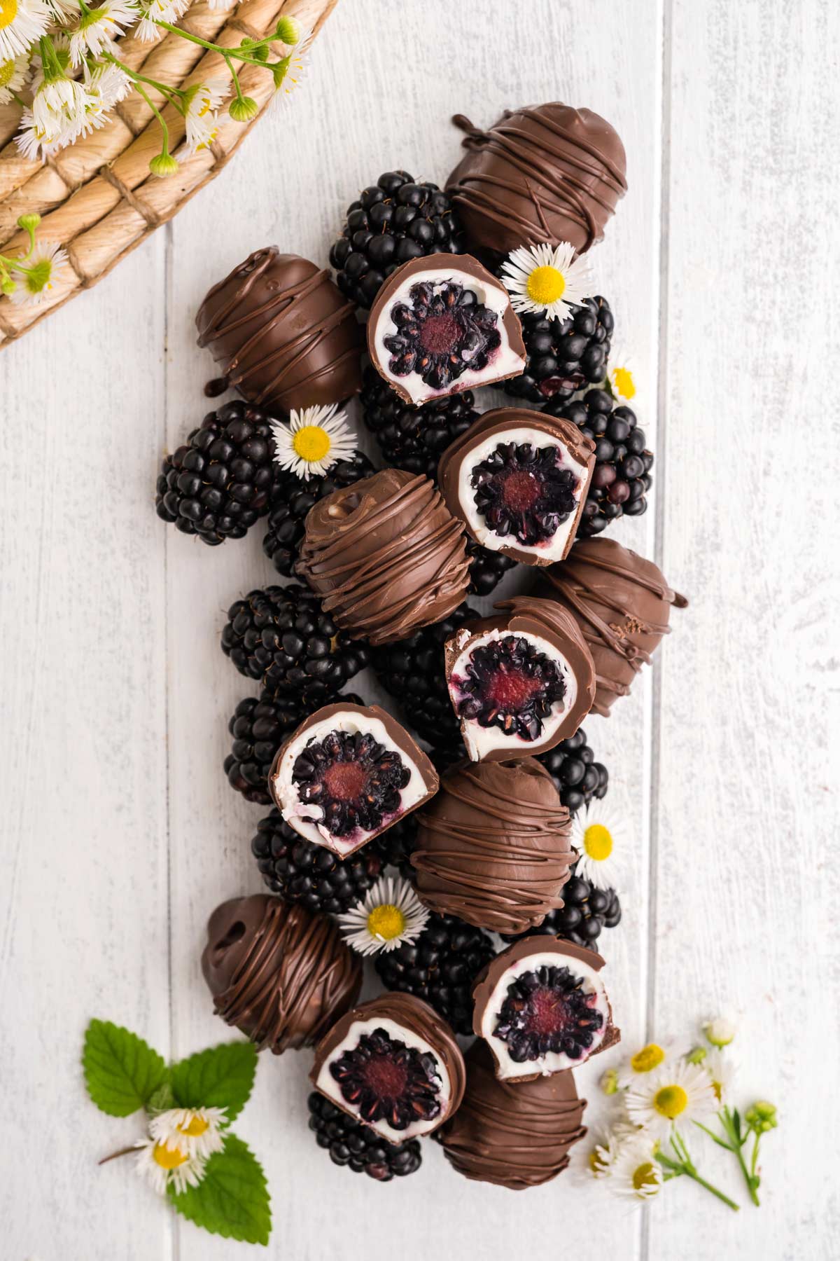 Chocolate dipped blackberries in a long pile on the table with some cut in half to show the inside.