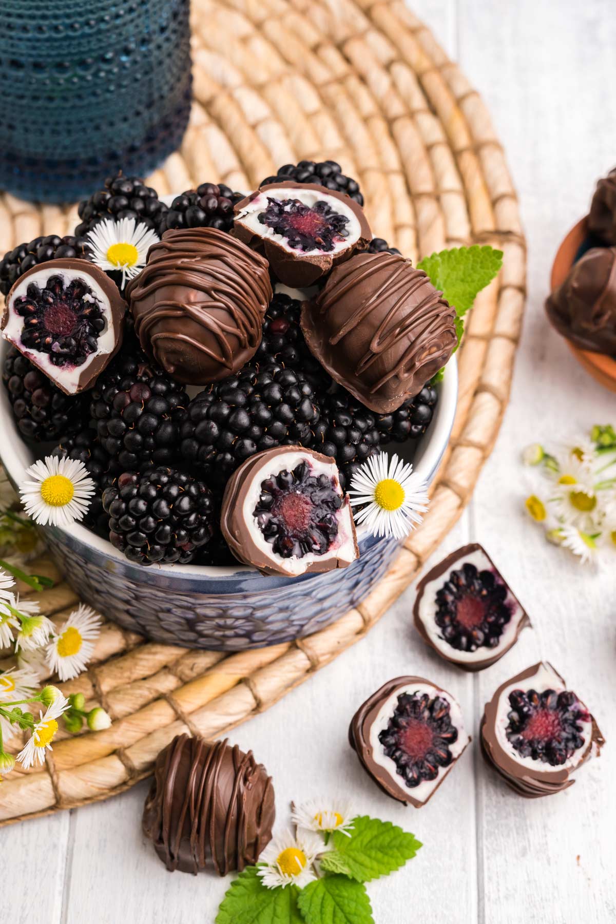 A bowl of chocolate covered blackberries with some cut in half and on the table.