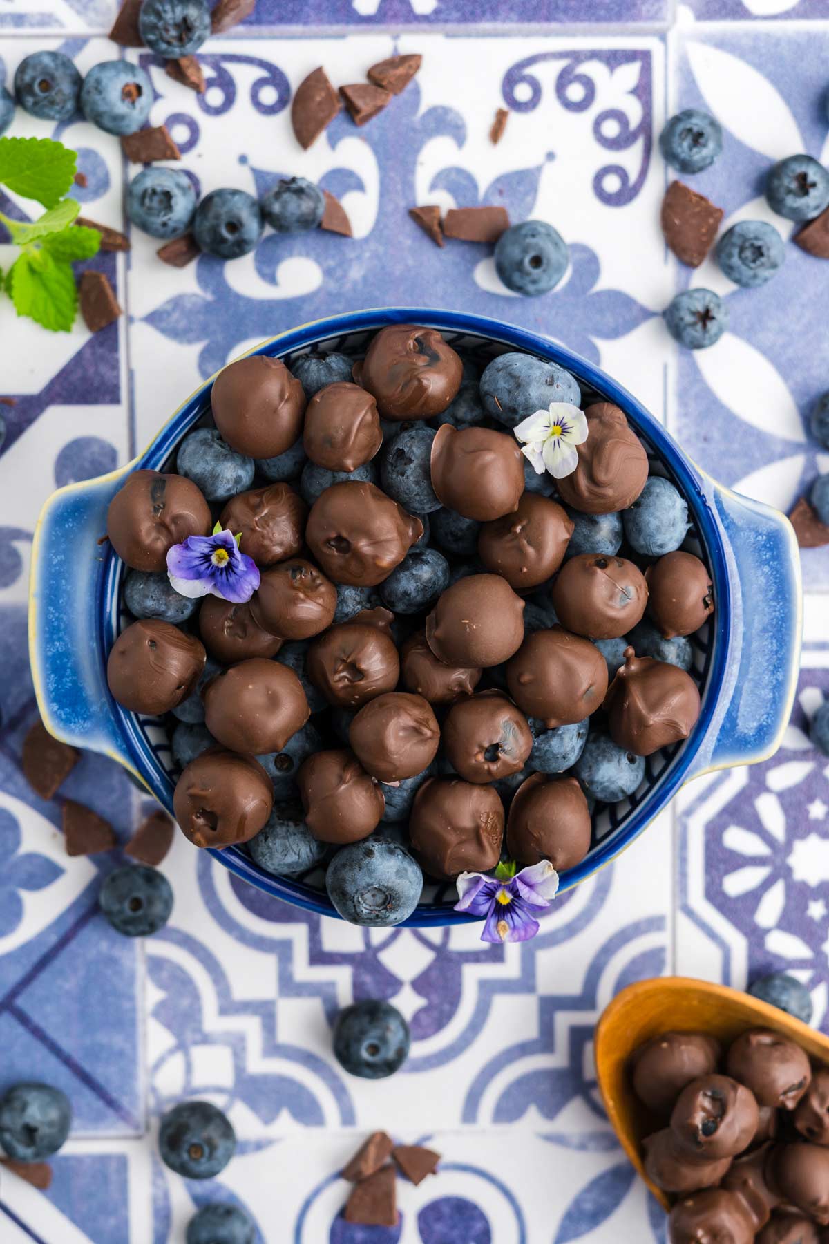 A bowl of chocolate covered blueberries on the table on a blue and white tile background.