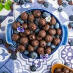 A bowl of chocolate covered blueberries and plain blueberries in a blue bowl together.