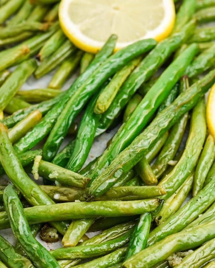 Close up of roasted green beans garnished with lemon slices.