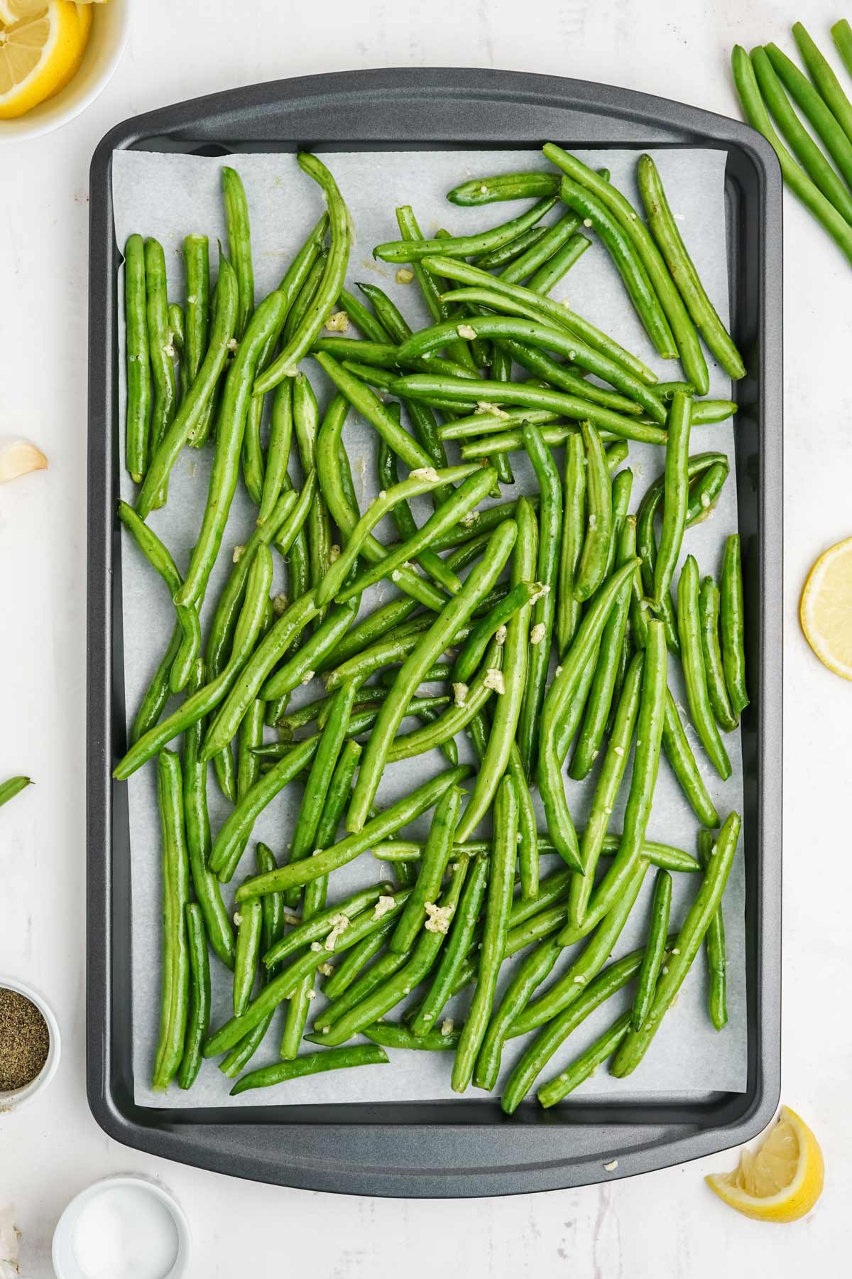 Green beans tossed in butter mixture spread out on a baking pan.