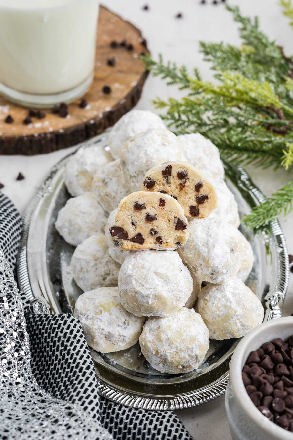 Chocolate chip snowball cookies on an oval platter with one cut in half to show the inside. 