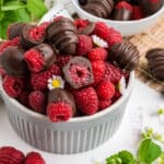 Chocolate covered raspberries in a bowl with one cut in half to show the inside.