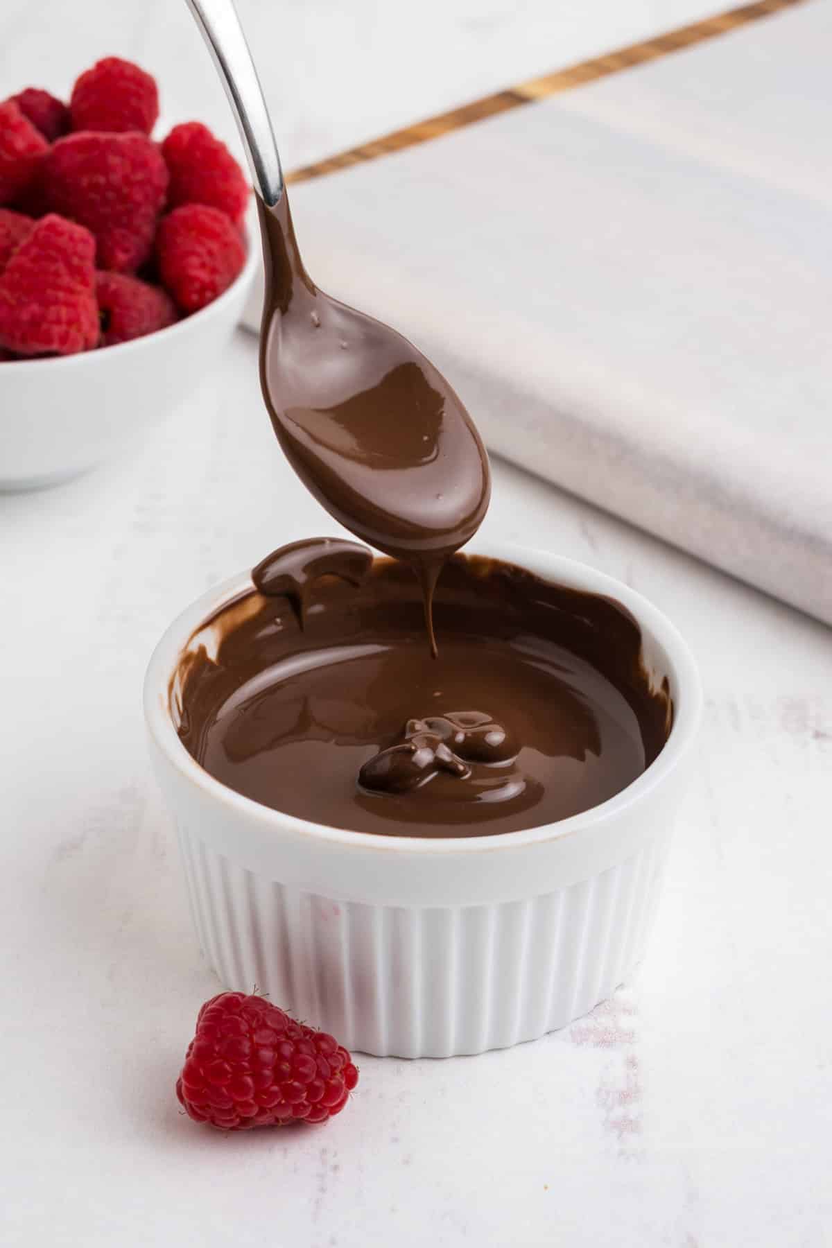 Melted chocolate in a bowl with a spoon lifting some out to drip back into it.