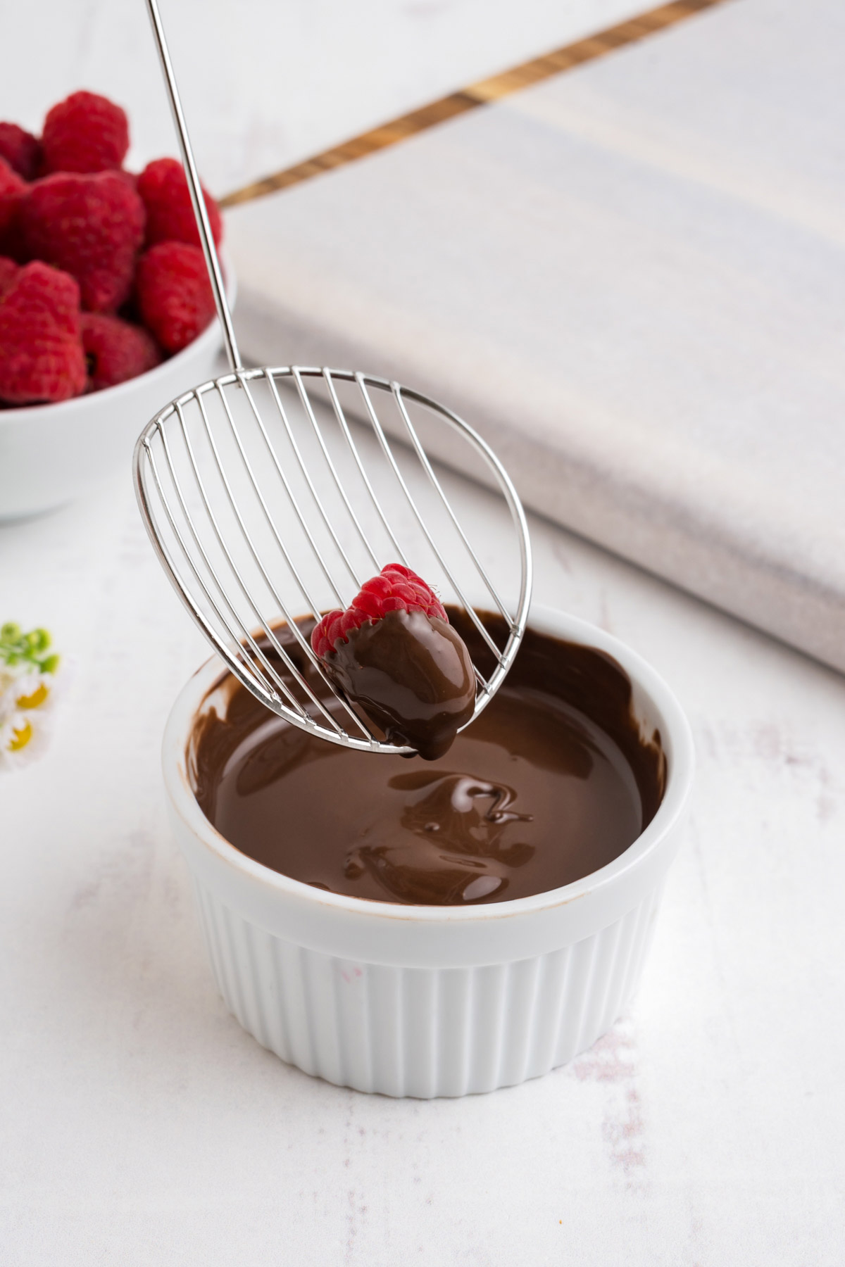 Using a metal slotted spoon to dip a raspberry in chocolate.