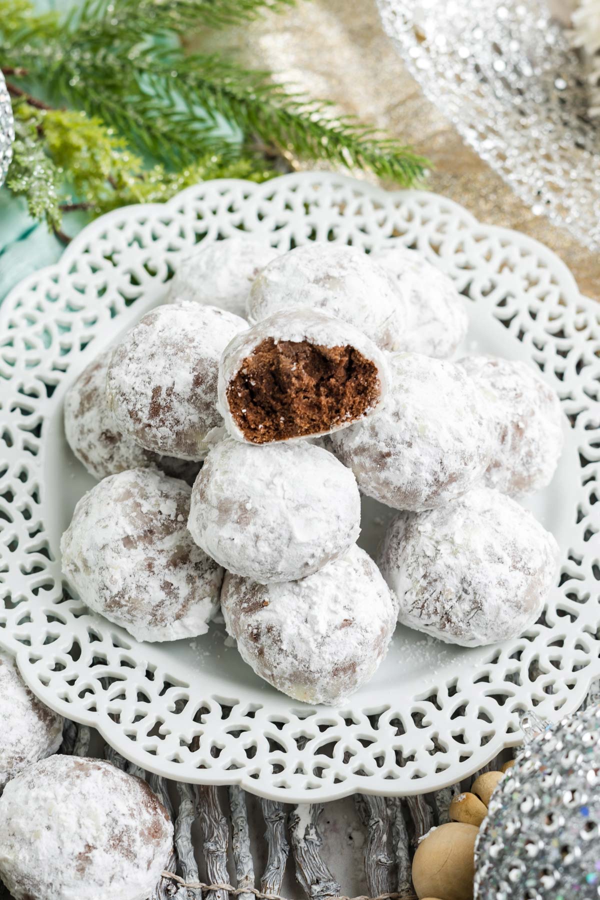 A white plate with a laced edge piled high with chocolate snowball cookies.