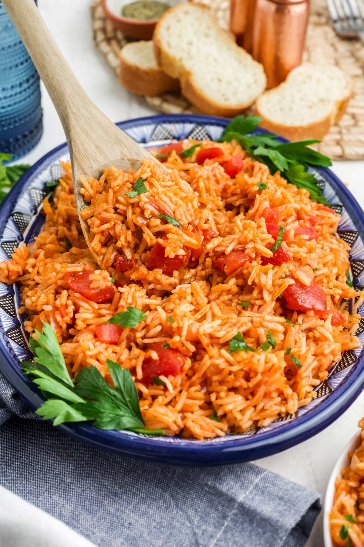 Tomato rice served up in a white and blue platter with a wooden spoon lifting up a bit.