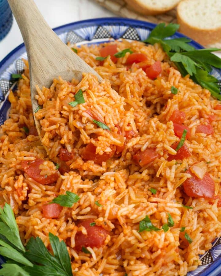 A bowl of tomato rice with a wooden spoon lifting up a portion.