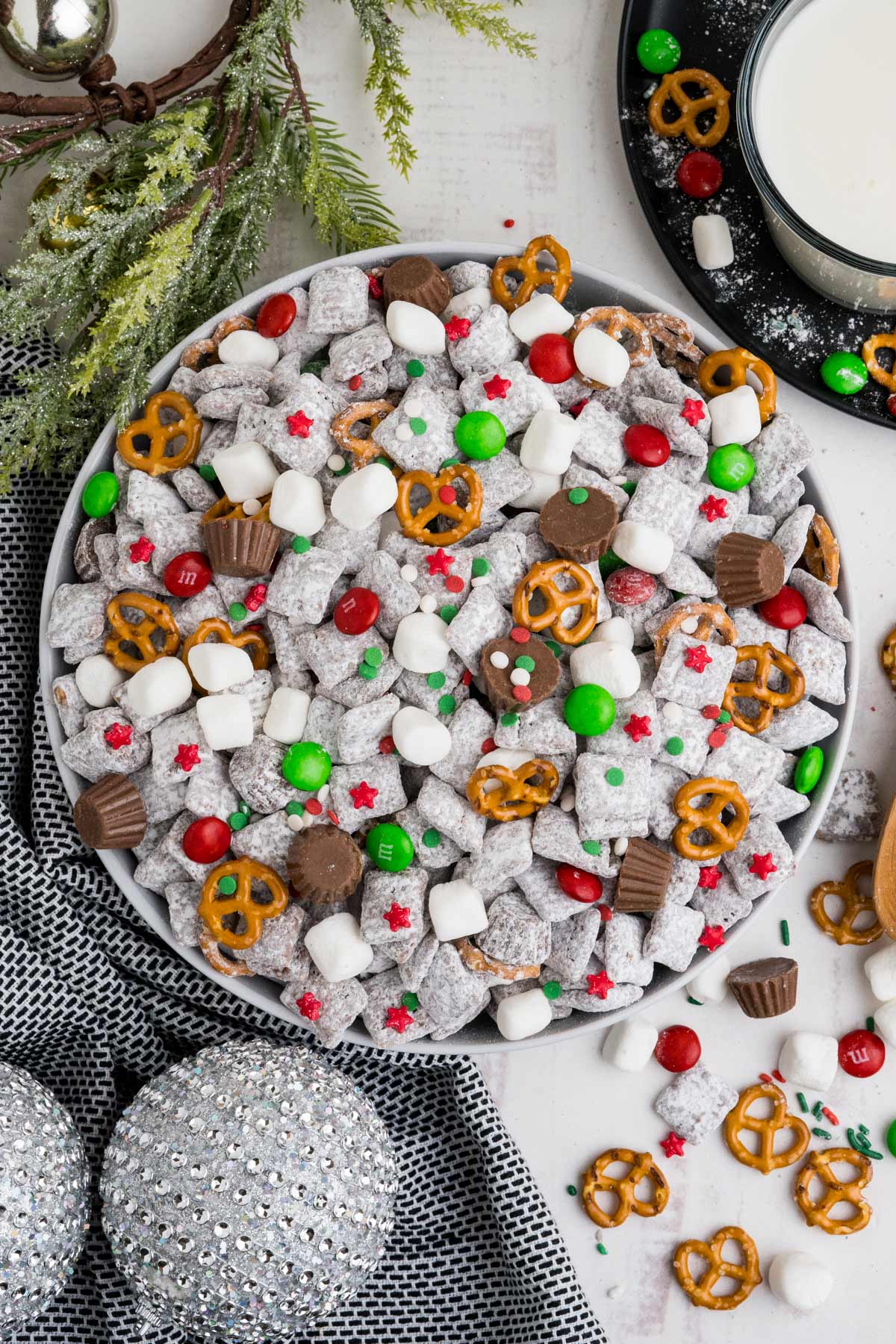 A bowl of Christmas muddy buddies on the table with ingredients scattered on the table.