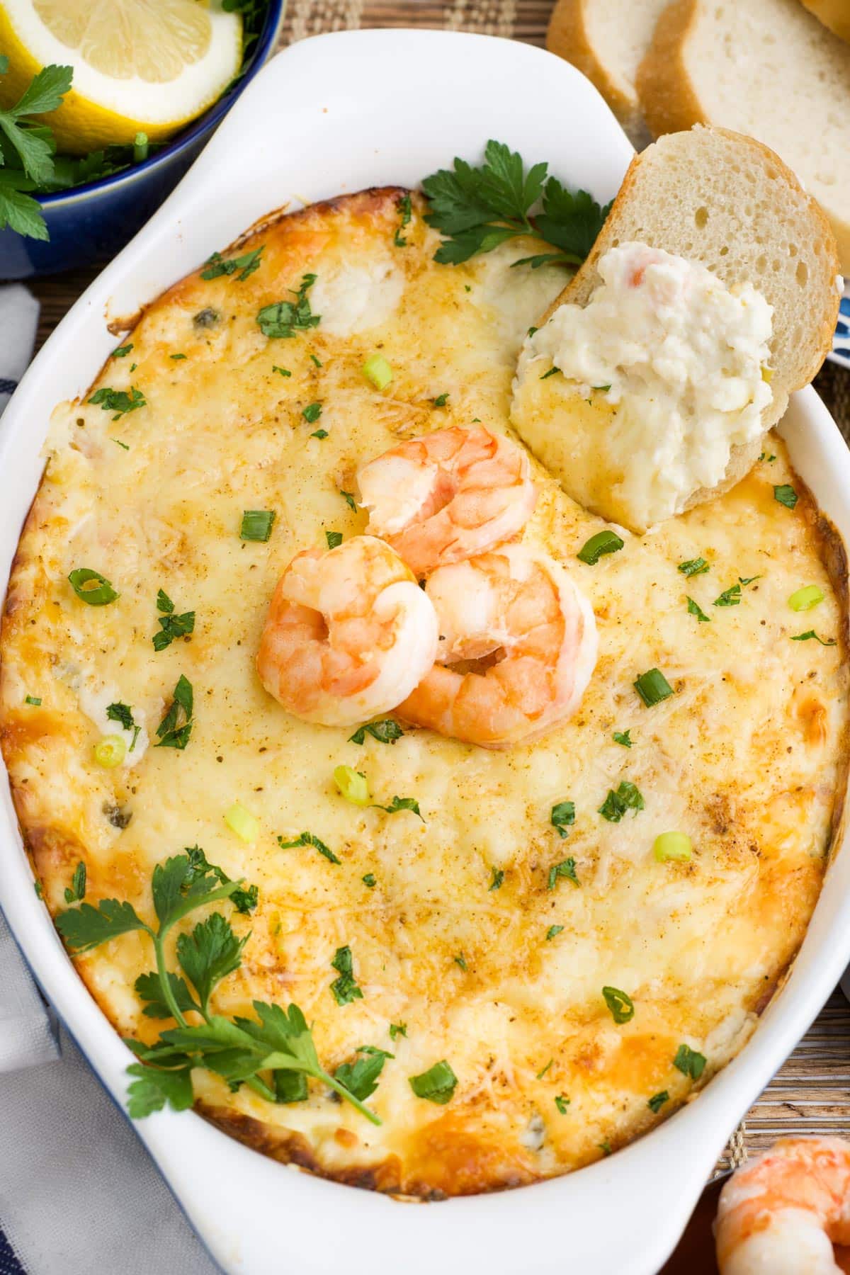 Baked shrimp dip in a casserole dish on the table topped with three shrimp and parsley.