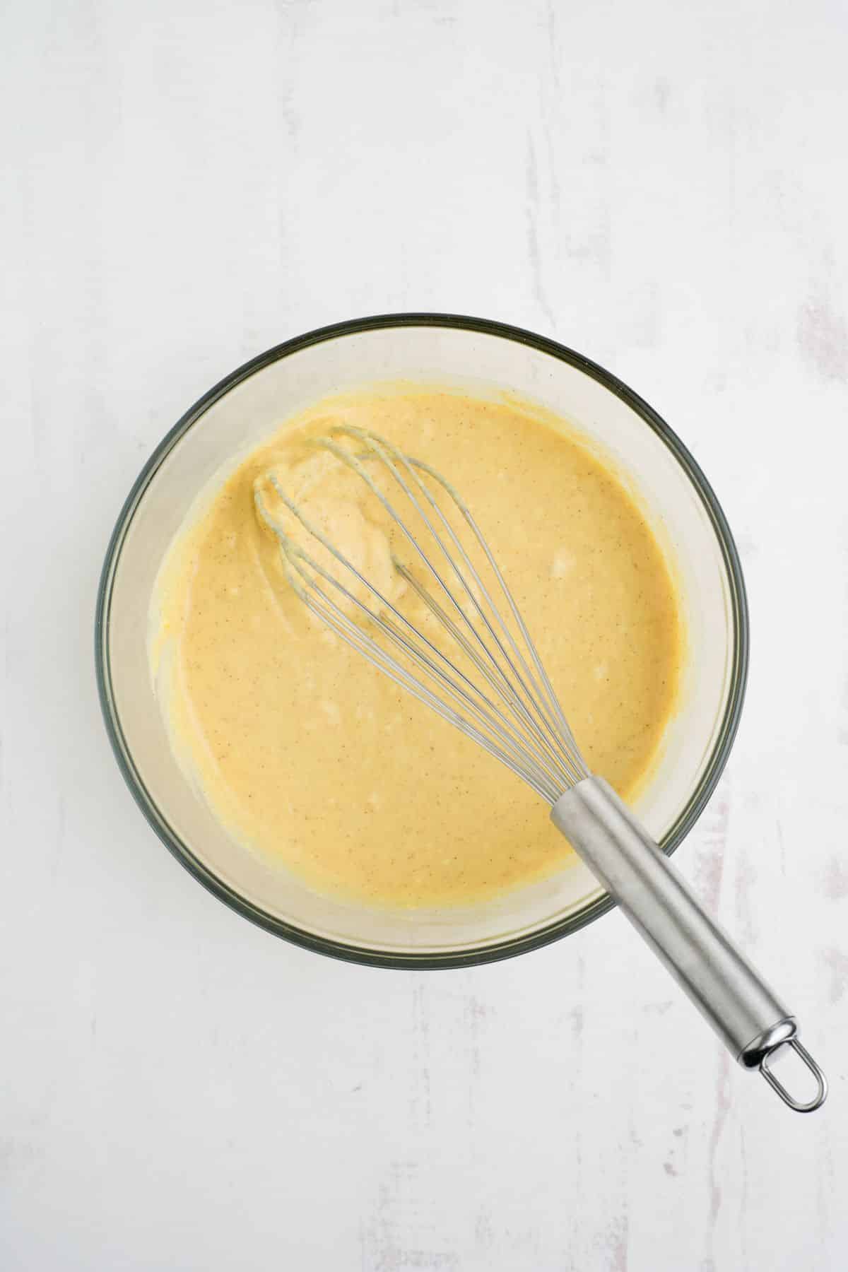 Ingredients mixed together in a bowl to make eggnog dip with a whisk in the bowl.