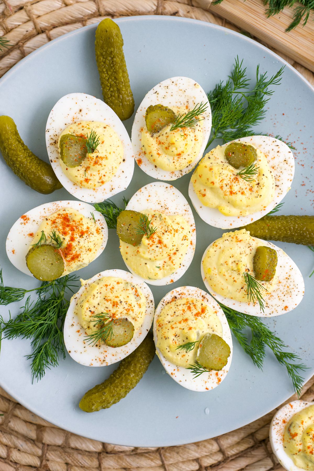 Dill pickle deviled eggs on a blue plate garnished with baby dill pickles and fresh herbs.