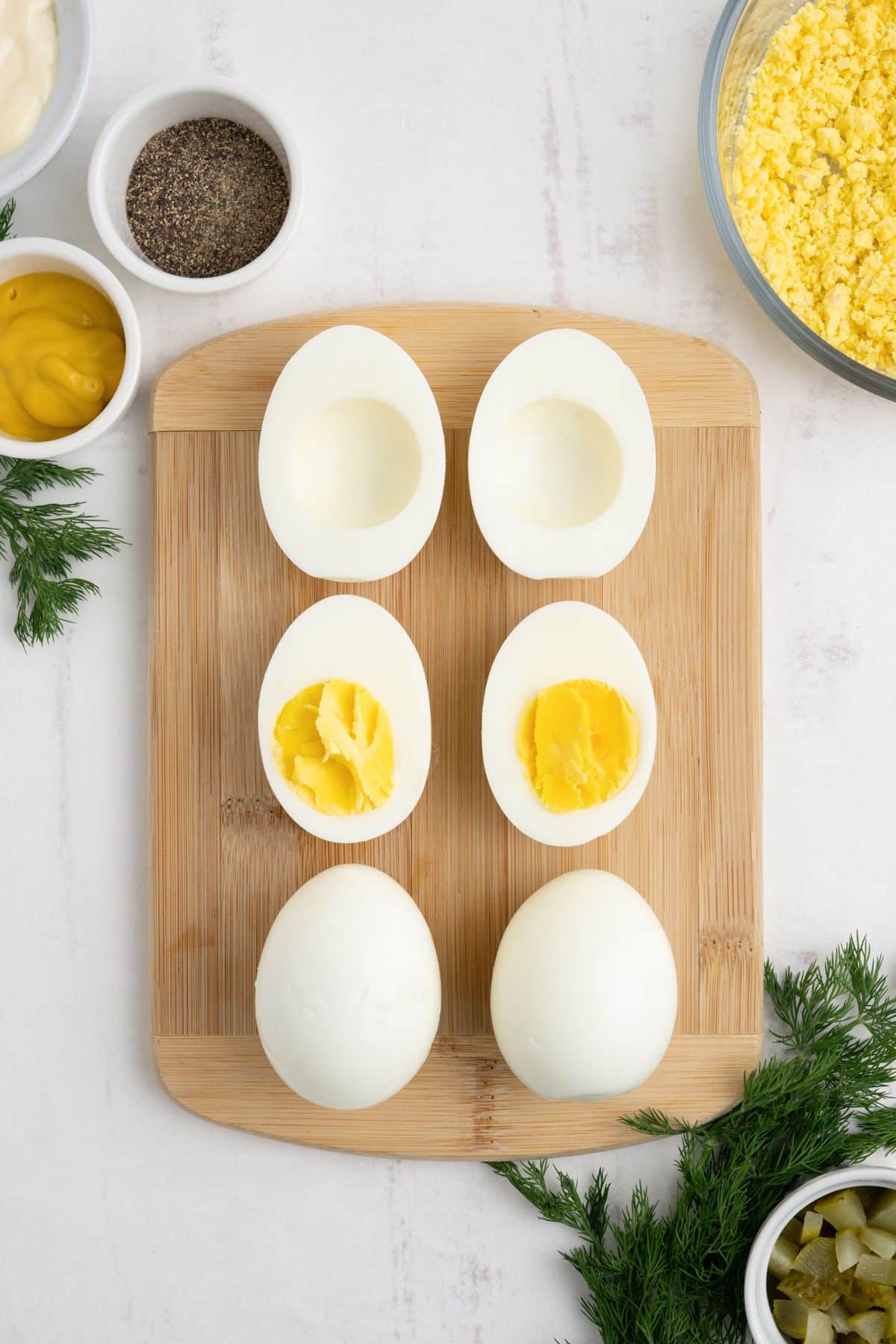Eggs cut in half on a cutting board with some of the yolks removed.